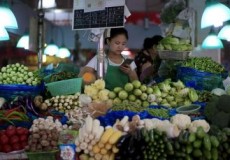 A vegetable vendor looks at her mobile phone at a market in Shanghai